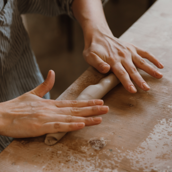 hands shaping clay, rolling it on a work table