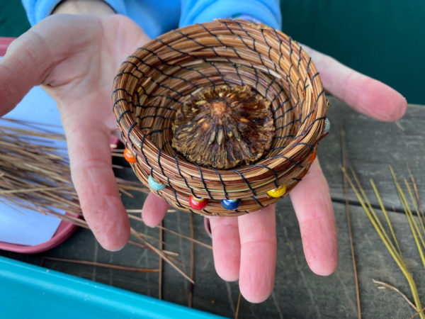 hand holding a handwoven Pine needle basket