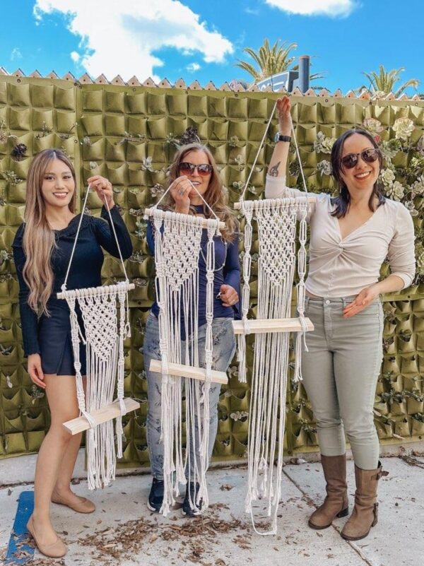 3 women holding up handmade macrame' wooden shelf wall hangings