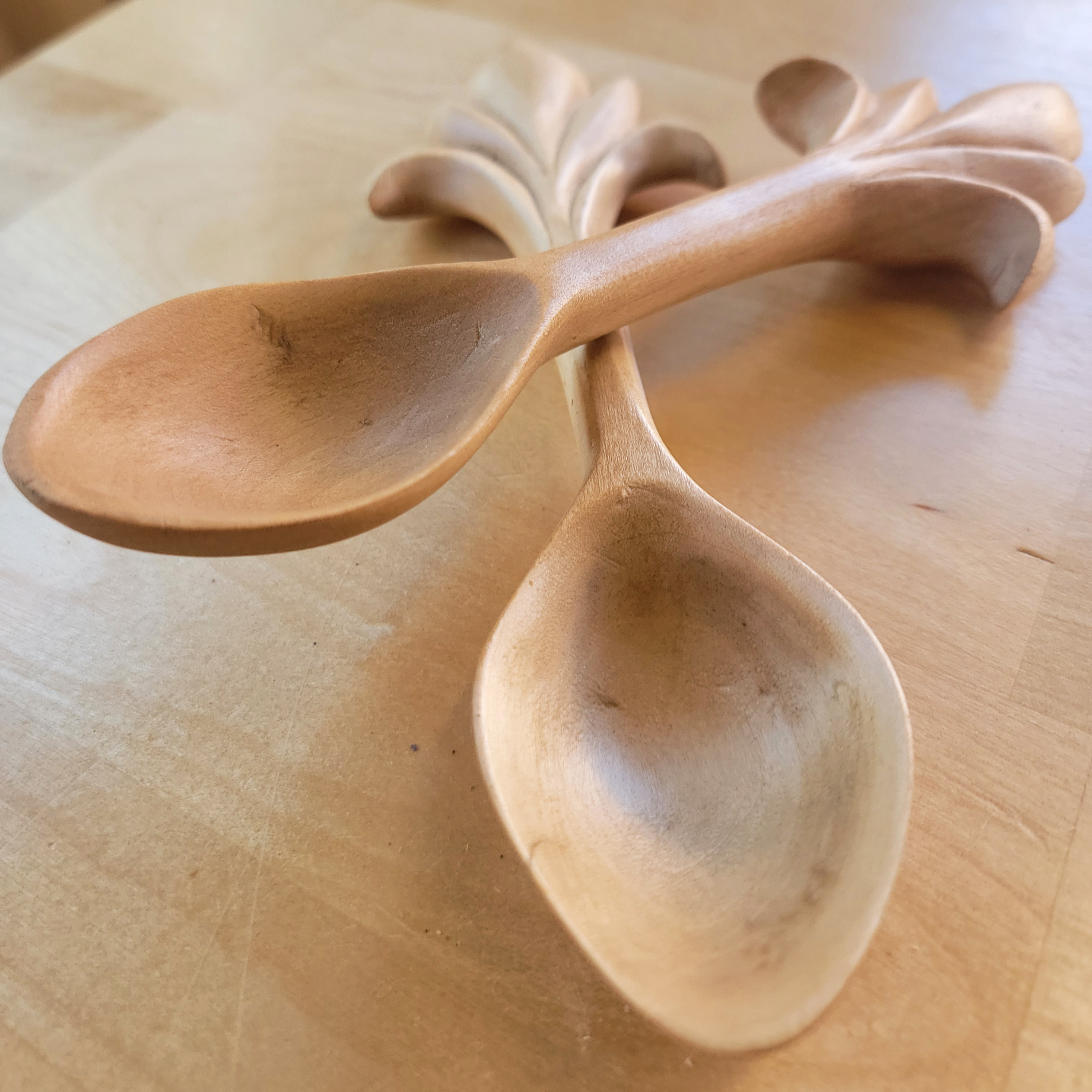 close up of two handcarved spoons with decorative handles lying side by side on table