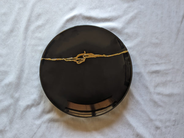 black plate with golden kintsugi repair work resting on white table