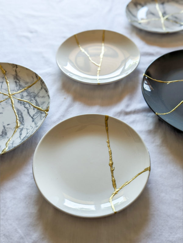 a variety of plates repaired with kintsugi golden repair work resting on white table