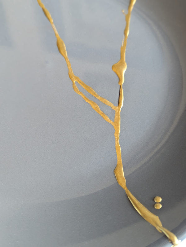 closeup of kintsugi golden repair work on grey plate