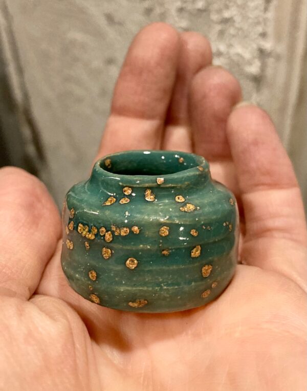close up of tiny green speckled clay pot in hand