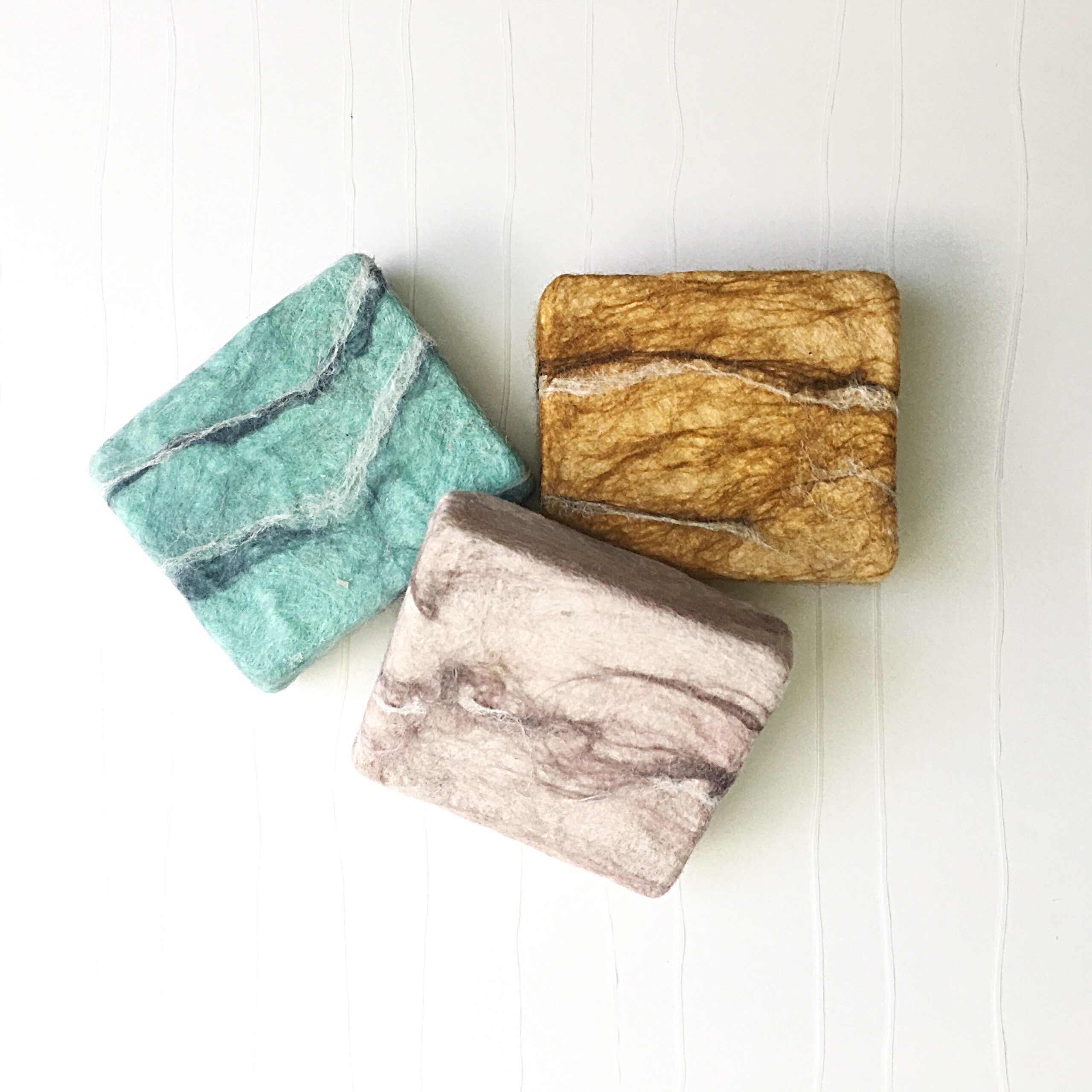 three bars of handmade wet felted soap in blue, pink and gold fibers