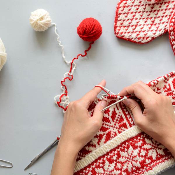 hands knitting a red and white sweater