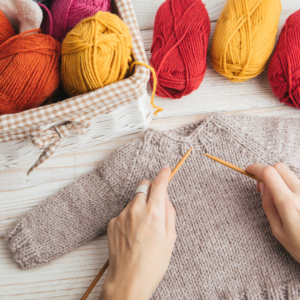 hands working on a hand knit sweater with yarn in background