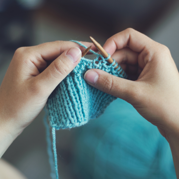 two hands holding knitting needles and knitting blue fabric