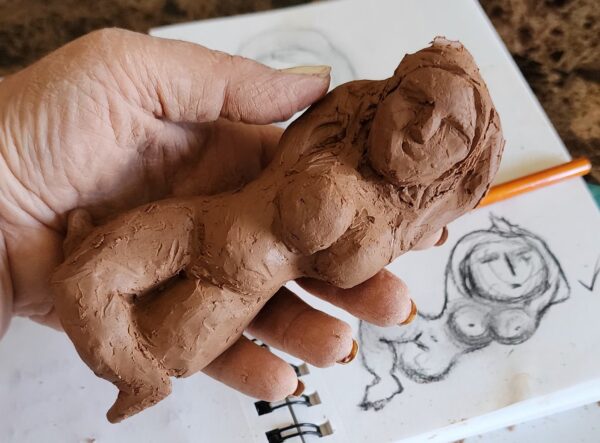 handmade clay figure of a woman sculpted and in hand with a sketch in the background