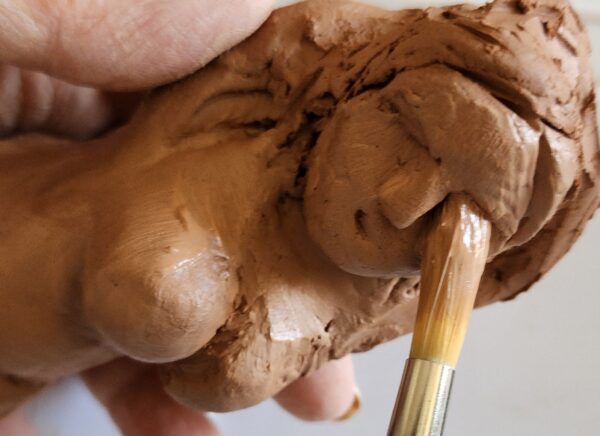 handmade clay figure of a woman's face in progress with a clay brush