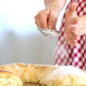 woman sprinkling powdered sugar on austrian strudel