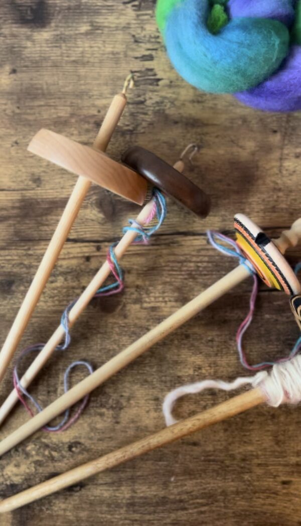 drop spindles laying on wooden table with wool being spun
