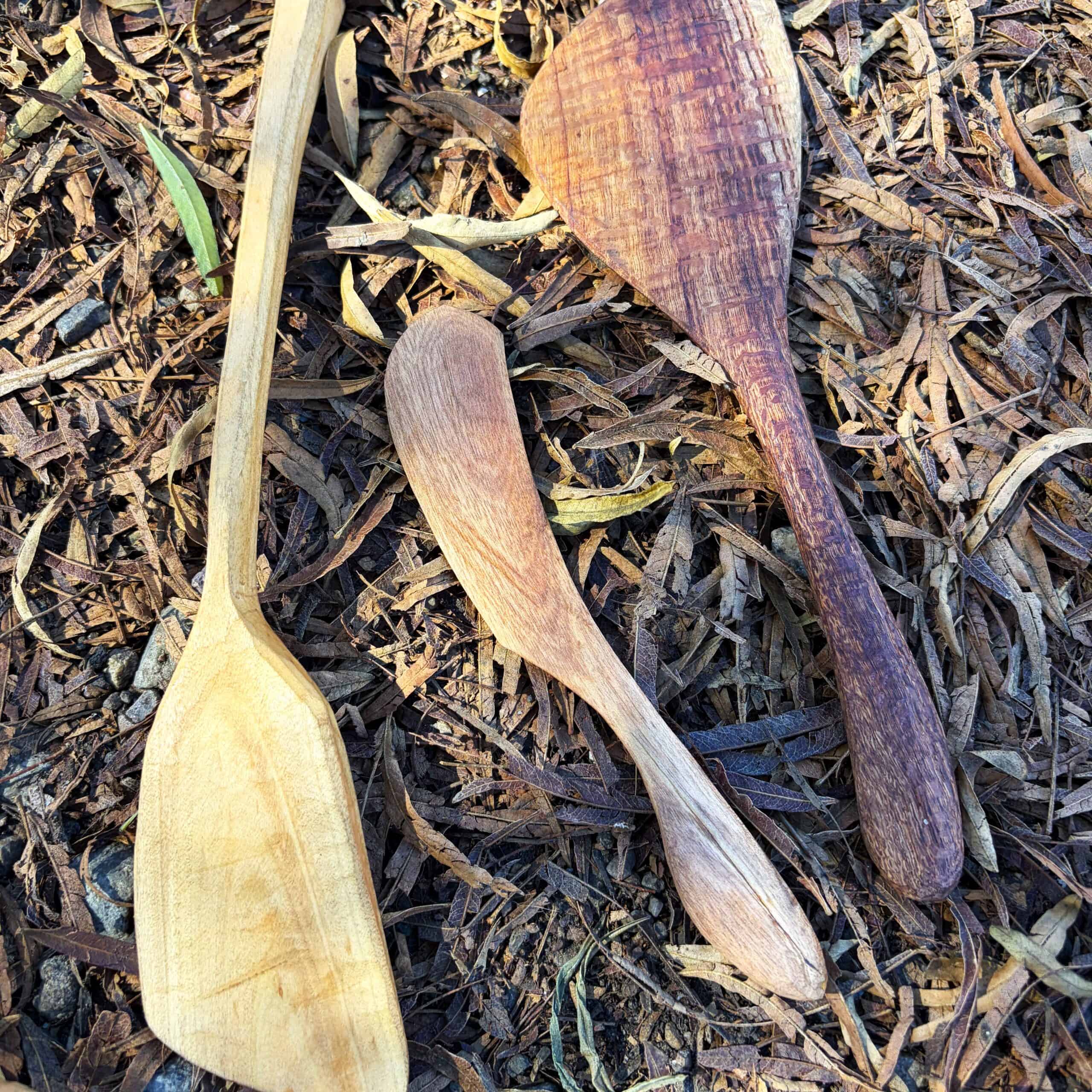 handcarved wooden spaturals and cheese spreaders resting on earth